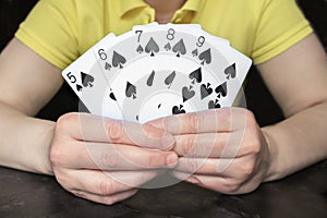 Close-up of hands holding five cards with a poker Straight Flush from a row of spades