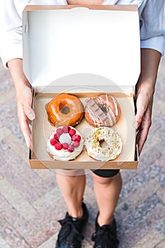 Close up hands holding four pieces of totally different colorful and delicious looking donuts in ecological carton box. appetising