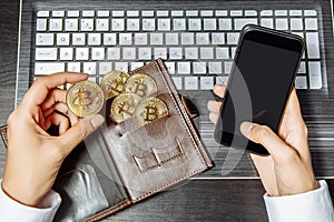 Close-up of hands holding a gold coin bitcoin and smartphone. Worldwide cryptocurrency and digital payment concepts.