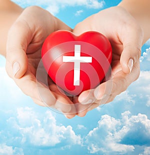 Close up of hands holding heart with cross symbol