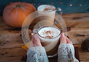 Close-up of hands holding pumpkin spice latte in glass cup, on wooden background