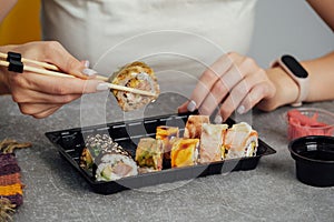 Close-up of hands holding sushi roll with chopsticks.