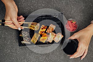 Close-up of hands holding sushi roll with chopsticks. Top view