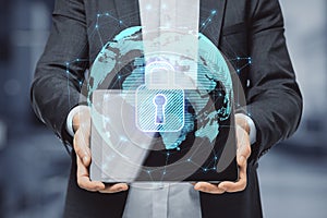 Close up of hands holding tablet with abstract glowing globe hologram with security padlock icon on blurry office interior room