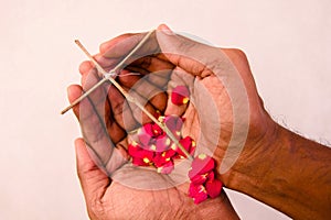 Close up of the hands of a holding a wood cross with red rose petals