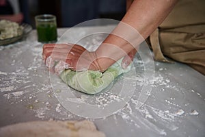 Close-up hands of a housewife kneading dough on the floured kitchen table, making dumplings for dinner