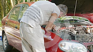 Close-up of hands of inexperienced man who approaches open hood of broken car and tries to repair it on his own