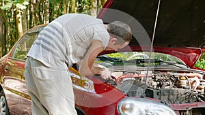 Close-up of hands of inexperienced man who approaches open hood of broken car and tries to repair it on his own