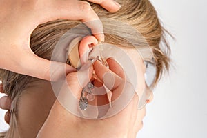 Close up of hands inserting a hearing aid in ear