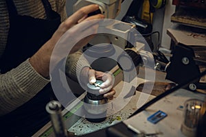 Close up hands of jeweller, goldsmiths making of golden cross with gemstone using professional tools.