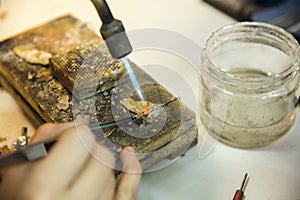 Close up hands of jeweller, goldsmiths making of golden ring with gemstone using professional tools.