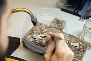 Close up hands of jeweller, goldsmiths making of golden ring with gemstone using professional tools.