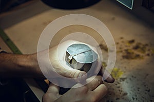 Close up hands of jeweller, goldsmiths making of golden ring with gemstone using professional tools.