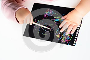 Close up of the hands of a little child drawing on magic scratch painting paper with drawing stick.