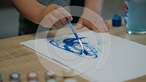Close-up of hands of little child draws with a brush and blue paint on a sheet of paper at home