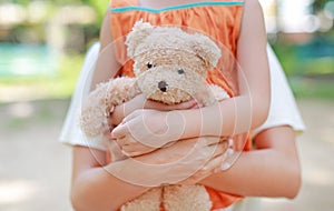 Close-up hands of little child girl and mom hugging teddy bear. Mother and daughter cuddle doll