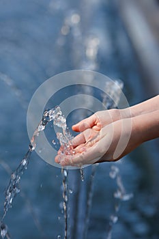 Close-up hands of a little girl catching clear blue water from a fountain