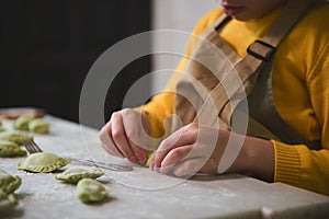 Close-up hands of a little kid girl in the rural kitchen, sculpts dumplings from dough with mashed potatoes filling