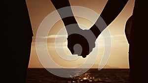 Close up hands of loving couple holding hands on backdrop of sun. Family at sunset on sea. Close up of man and woman