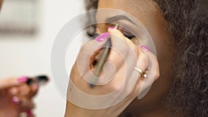 Close-up hands of makeup artist applying and correcting makeup on black african american model. Beauty and fashion