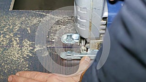 Close-up hands of a male builder cuts a wooden with an electric jigsaw.