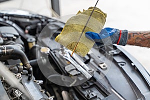 Close up hands of a male car mechanic checking car oil with engine in the background