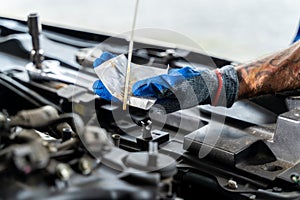 Close up hands of a male car mechanic checking car oil with engine in the background