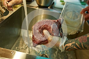 Close up of hands of male cook cleaning the raw pork under tap water for cooking