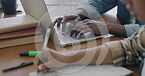 Close-up of hands male and female writing in notebook and typing with laptop computer studying on campus at desk