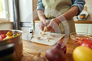 Close up of hands of man in apron peeling garlic while preparing healthy meal, soup in the kitchen. Cooking at home