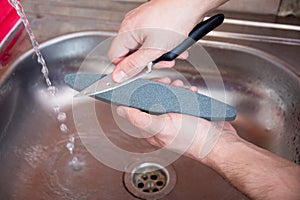 Close-up hands of a man carefully sharpen a knife under a stream of water on a grindstone. Home household sharpening