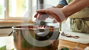 Close up of hands of man, chef cook adding onion to the pot with chopped vegetables while preparing a meal in the