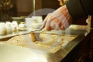 Close up hands of a man cooking turkish coffee on hot golden sand.