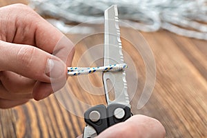 Close-up hands of man cuts the rope using multi tool with serrated blade.