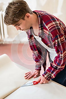 Close-up of the hands of a man cutting a new wallpaper sheet