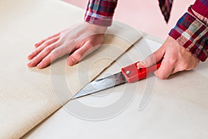 Close-up of the hands of a man cutting a new wallpaper sheet dur