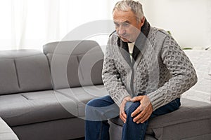 close up hands man with his knee joint pain in sofa, pain in the elderly, health care. Grandfather with knee pain