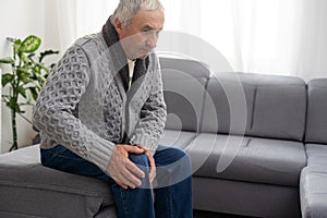 close up hands man with his knee joint pain in sofa, pain in the elderly, health care. Grandfather with knee pain