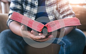 Close up hands of man holding bible and reading on sofa at home. christian concept