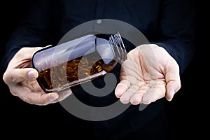 A close-up of the hands of a man holding a jar of fish oil capsules pours capsules on his palm