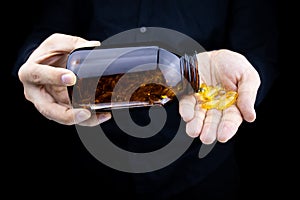 A close-up of the hands of a man holding a jar of fish oil capsules pours capsules on his palm