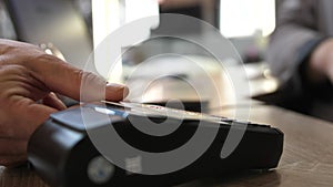 Close up hands of man making payment with credit card machine terminal while swiping debit card to pay the bill. NFC