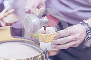 Close-up of hands of man making traditional turkish coffee in copper turk on hot sand, pours into disposable paper cup