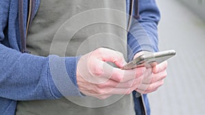 Close-up hands man typing message on mobile phone outdoors at city street. Young male chatting on phone in slow motion.