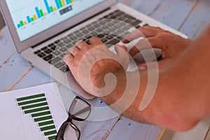 Close up of hands of man using a laptop - business man looking at the graphs on the screen and on the table