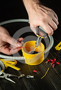 Close-up of the hands of a master electrician during work. Cutting the white wire in the yellow junction box. Idea for