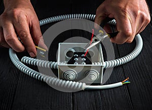 Close-up of hands of master electrician during work. Installing a cable or wire to gray junction box. Electrical connection in the