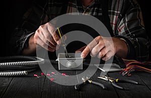 Close-up of hands of a master electrician during work. Installing a cable or wire to grey junction box