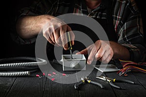 Close-up of hands of a master electrician during work. Installing a cable or wire to grey junction box. Idea for the installation