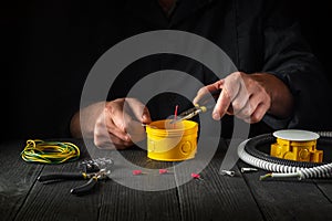 Close-up of hands of a master electrician during work. Installing a cable or wire to yellow junction box. Free advertising space